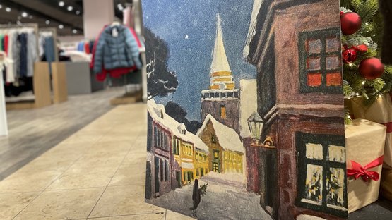 Rechts im Vordergrund eine Postkarte mit einem gemalten Motiv. Im Hintergrund Kleidung