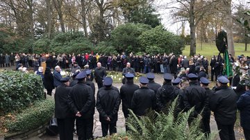 Eine große Anzahl Menschen stehen im Halbkreis um ein Rednerpult.