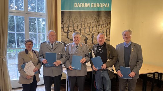 Links eine Frau, daneben vier Männer. Teilweise tragen sie Uniform. In den Händen halten sie Mappen.