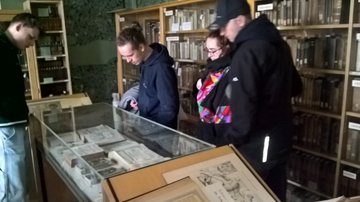 Vier Personen stehen in einer Bibliothek um eine Glasvitrine und schauen sich historische Dokumente an.